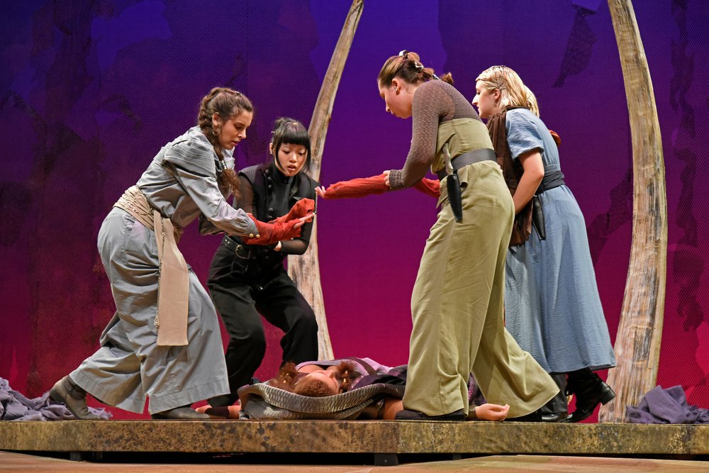 Four people put on bloody gloves over a dead Julius Caesar