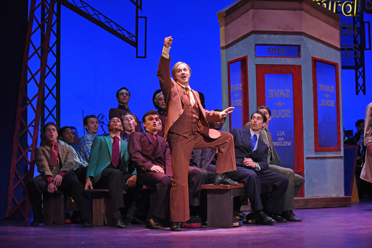 A person stands with a leg up on a church pew, as others look at them from behind