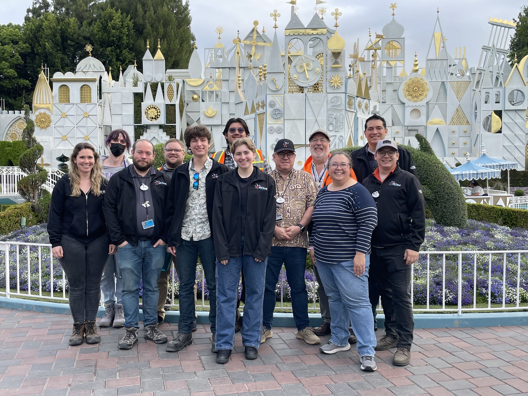a group of Imagineers poses in front of Disneyland's it's a small world to celebrate the reopening