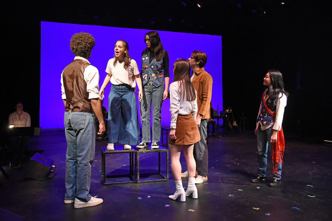 A group of students gathers around a girl speaking on an elevated platform
