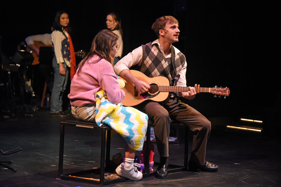 A man plays guitar as a girl sits next to him with a stuffed duck